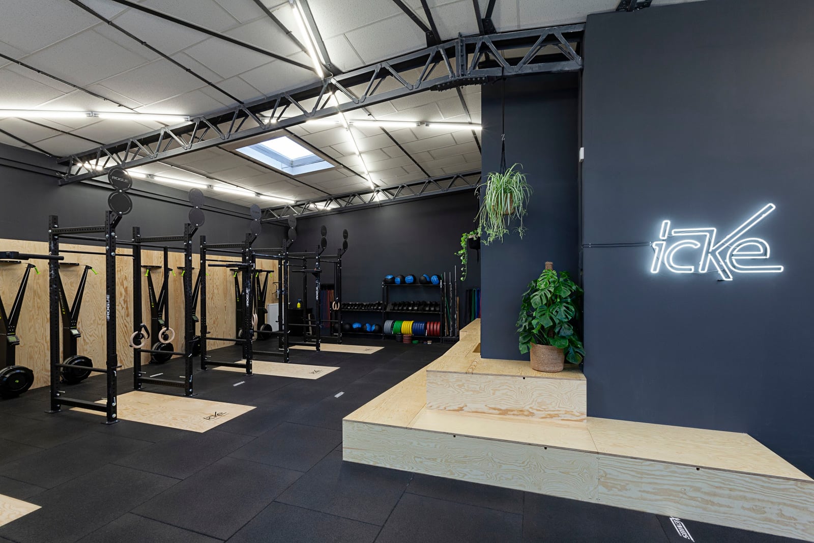 Trainingsfläche von CrossFit ICKE in Berlin-Schöneberg: Racks, Hantelscheiben und Holzplattform unter dem beleuchteten ICKE-Schriftzug
