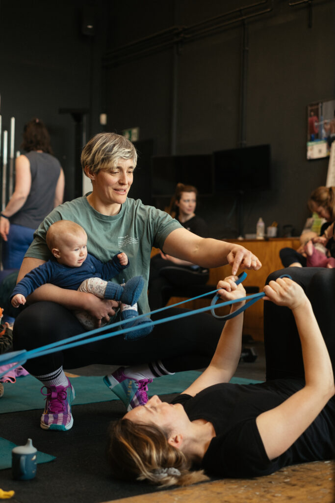 trainerin-coaching-mama-baby-kurs-crossfit-icke-berlin. Trainerin coacht Mama beim postnatalem Fitnesskurs mit Baby bei CrossFit Icke Berlin